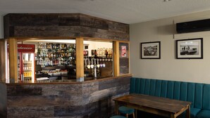 Una zona de bar con mostrador de madera, taburetes y un área de asientos con un banco tapizado en azul.