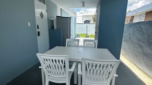 A modern outdoor dining area with a white table and chairs, a ceiling fan, and a view of a basketball court through an open door. - Cozy in Cabo offers a beautiful stay in Cabo Rojo Puerto Rico 10m from beach.  (Cabo Rojo)