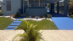 A modern two-story house with a flat roof, a covered front porch, and a small front yard with a palm tree and stepping stones. - Cozy in Cabo offers a beautiful stay in Cabo Rojo Puerto Rico 10m from beach.  (Cabo Rojo)