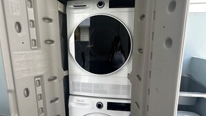 A compact, enclosed laundry room with two stacked washers and dryers, featuring a control panel and a mirror. - Cozy in Cabo offers a beautiful stay in Cabo Rojo Puerto Rico 10m from beach.  (Cabo Rojo)