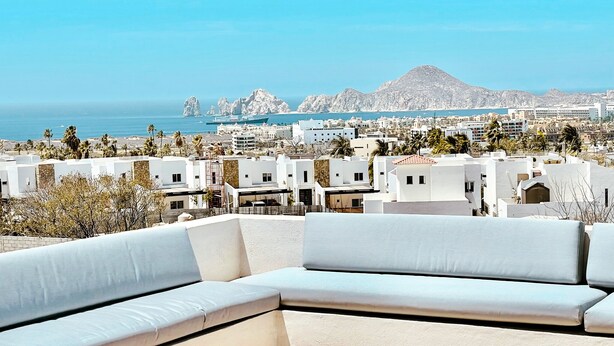 A modern outdoor seating area with a view of a coastal town and mountains. - Ocean-View Rooftop Oasis- Pool, Hot Tub, Fire Pits, 5 minutes to beach & DT Cabo (El Tezal)