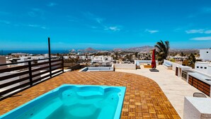 A rooftop terrace with a hot tub, seating area, and a view of the city and sea. - Ocean-View Rooftop Oasis- Pool, Hot Tub, Fire Pits, 5 minutes to beach & DT Cabo (El Tezal)