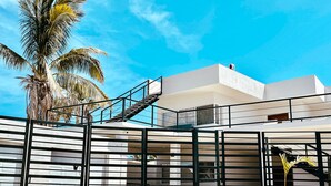 A modern building with a staircase leading to a balcony, surrounded by palm trees and a clear blue sky. - Ocean-View Rooftop Oasis- Pool, Hot Tub, Fire Pits, 5 minutes to beach & DT Cabo (El Tezal)