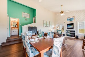 Un coin repas avec une table et des chaises en bois, une cuisine à l’arrière-plan et un ventilateur de plafond.