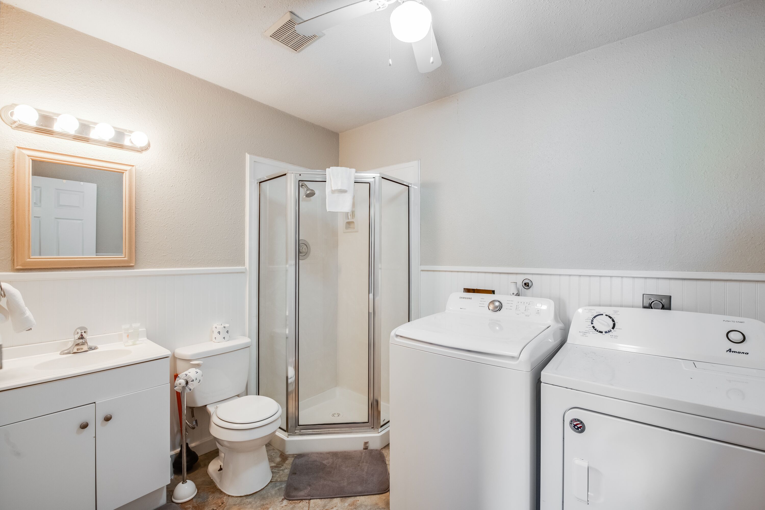 A bathroom with a shower, toilet, sink, and two washing machines.