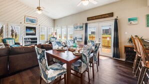A dining area with a wooden table, chairs with leaf-patterned cushions, and a ceiling fan. - Walk to Beach! Boardwalk to Beach, Shared Pool, Pets OK! (Port Aransas)