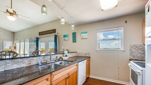 A modern kitchen with wooden cabinets, a granite countertop, a dishwasher, and a large window. - Walk to Beach! Boardwalk to Beach, Shared Pool, Pets OK! (Port Aransas)