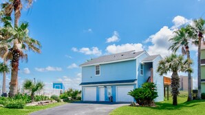 A two-story residential building with a blue exterior, a front driveway, and palm trees. - Walk to Beach! Boardwalk to Beach, Shared Pool, Pets OK! (Port Aransas)