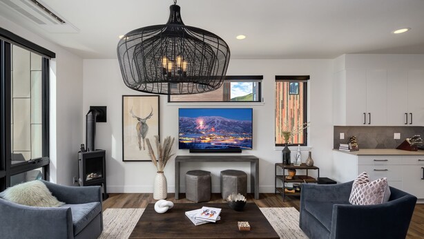 A modern living room with a fireplace, two grey sofas, a coffee table with magazines, and a large TV screen displaying a cityscape. - Luxury Townhouse with Rooftop Deck & Hot Tub, Close to Skiing - Skyline Retreat (Steamboat Springs)