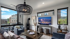 A modern living room with a large TV, comfortable seating, and a view of the city. - Luxury Townhouse with Rooftop Deck & Hot Tub, Close to Skiing - Skyline Retreat (Steamboat Springs)