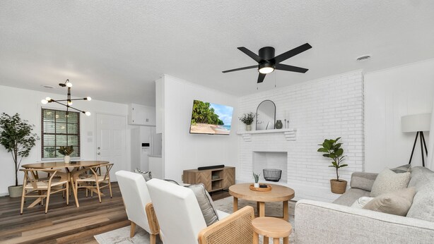 Un salon moderne avec une cheminée en briques blanches, un ventilateur de plafond et un coin repas doté de meubles en bois.
