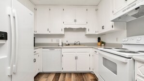 Une cuisine avec des meubles blancs, un lave-vaisselle, un four et une cuisinière.