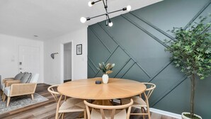 Un coin repas avec une table ronde en bois, des chaises en osier, une plante en pot et un luminaire moderne.