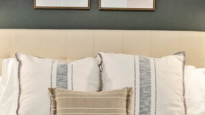 Un lit bien fait, avec du linge de lit blanc et des oreillers à rayures, et une œuvre d’art encadrée accrochée au mur au-dessus.