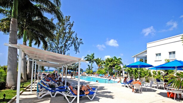 A poolside area with lounge chairs and umbrellas, surrounded by palm trees and a clear sky. - Amazing pool and nearby beach - Bliss (Sunset Crest)