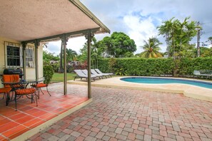 Un patio couvert avec une piscine, des chaises longues et un espace barbecue.