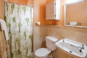 A bathroom with a toilet, sink, and shower curtain with a tropical pattern.