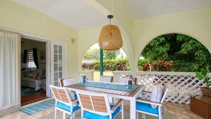 An outdoor patio with a table and chairs, a hanging light fixture, and a view of greenery. - Large pool, gardens and close to beach - Aqua Bliss (Sunset Crest)