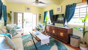 A living room with a sofa, TV, wooden cabinet, and potted plants. - Large pool, gardens and close to beach - Aqua Bliss (Sunset Crest)