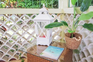 A wicker table with a glass top, a white lantern, a book titled 'In the Out of Barbecue', and a potted plant. - Large pool, gardens and close to beach - Aqua Bliss (Sunset Crest)