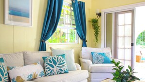A living room with a white sofa, teal cushions, and a glass coffee table. - Large pool, gardens and close to beach - Aqua Bliss (Sunset Crest)