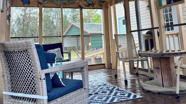A covered porch with wicker furniture, a ceiling fan, and a view of a green building. - Spring Warrior Pines
5 min to the ocean, boat ramp, and the WMA. (Perry)