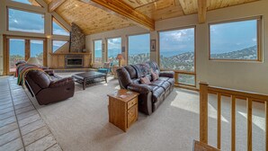 A spacious living room with a stone fireplace, leather sofas, and large windows offering mountain views. - Mountain Views• Private Hot Tub•Large Deck (Salida)
