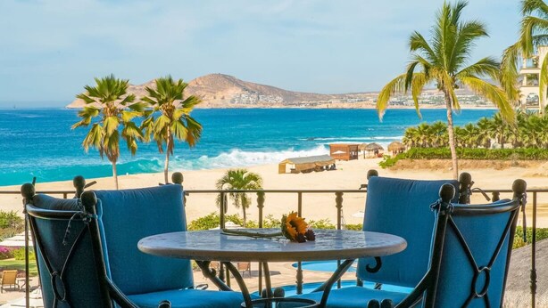 Une vue sur la mer avec une table et des chaises, des palmiers et une montagne en arrière-plan.