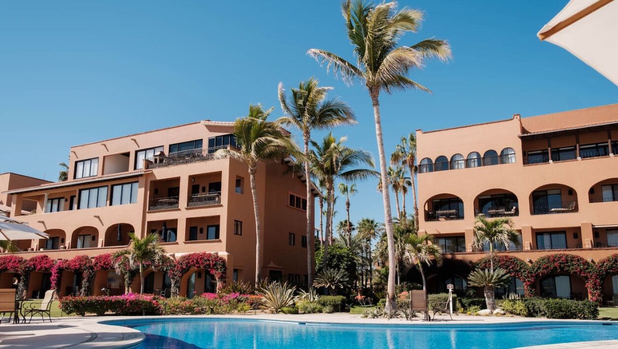 A hotel with a pool, palm trees, and a clear blue sky.