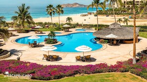 Une piscine d’hôtel avec des chaises longues et des parasols, entourée de palmiers et offrant une vue sur la plage.