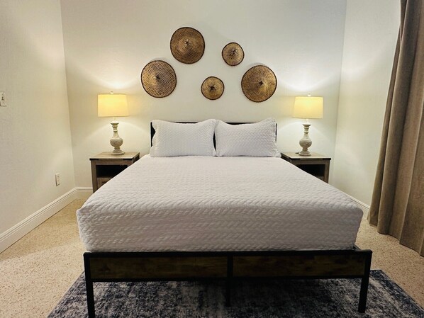 A neatly made bed with white linens, two bedside lamps, and a headboard with decorative wall art.