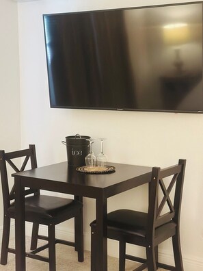 A dining area with a black table, two chairs, a black pot, and two wine glasses on a coaster.