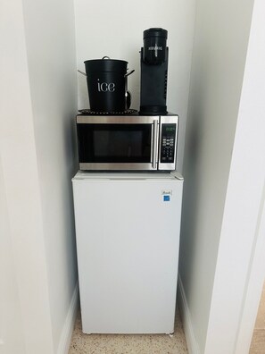 A compact kitchenette with a white refrigerator, a microwave, and a coffee maker.