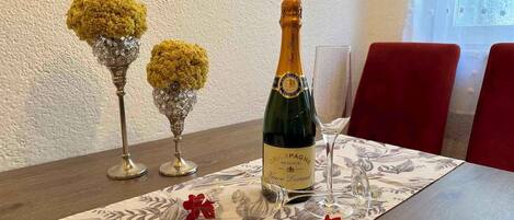 Une table dressée avec une bouteille de champagne, deux vases en cristal ornés de fleurs jaunes et un verre posé sur une nappe à motifs floraux.