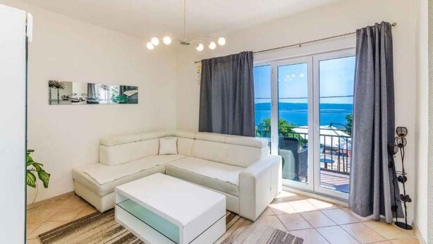 A modern living room with a white sectional sofa, a glass coffee table, and a large sliding glass door leading to a balcony with a view of the sea. - Holiday apartment with jacuzzi and sea view (Dramalj)