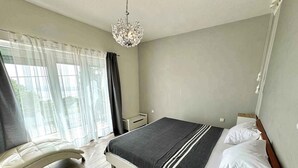 A modern bedroom with a bed, bedside tables, a chandelier, a sofa, and a view of the outdoors. - Holiday apartment with jacuzzi and sea view (Dramalj)