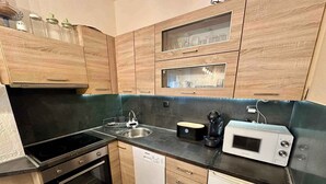 A compact kitchen with wooden cabinets, a black countertop, a built-in oven, a dishwasher, and a microwave. - Holiday apartment with jacuzzi and sea view (Dramalj)