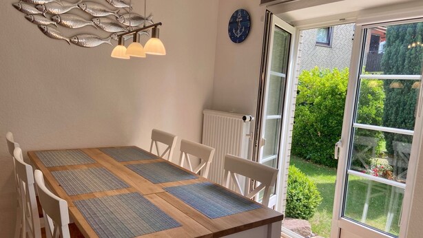 A dining area with a wooden table, white chairs, and a decorative fish wall hanging. - 5060 Saarstr. 8a, Deutschland (Dahme)