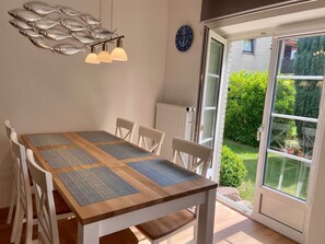 Un coin repas avec une table en bois, des chaises blanches et une décoration murale représentant des poissons.