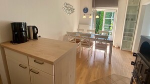 A compact kitchen with a wooden countertop, a coffee maker, and a dining area with white chairs and a table. - 5060 Saarstr. 8a, Deutschland (Dahme)