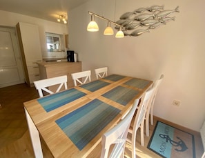 Zona pranzo con tavolo in legno e sedie bianche, una cucina sullo sfondo e un'opera d'arte decorativa a tema pesci.