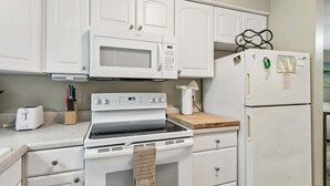 Une cuisine avec des meubles blancs, un four à micro-ondes, un four, un grille-pain et un réfrigérateur.