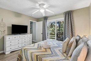 Ein Schlafzimmer mit einem Bett, einem Fernseher auf einer Kommode, einem Deckenventilator und Blick ins Freie.