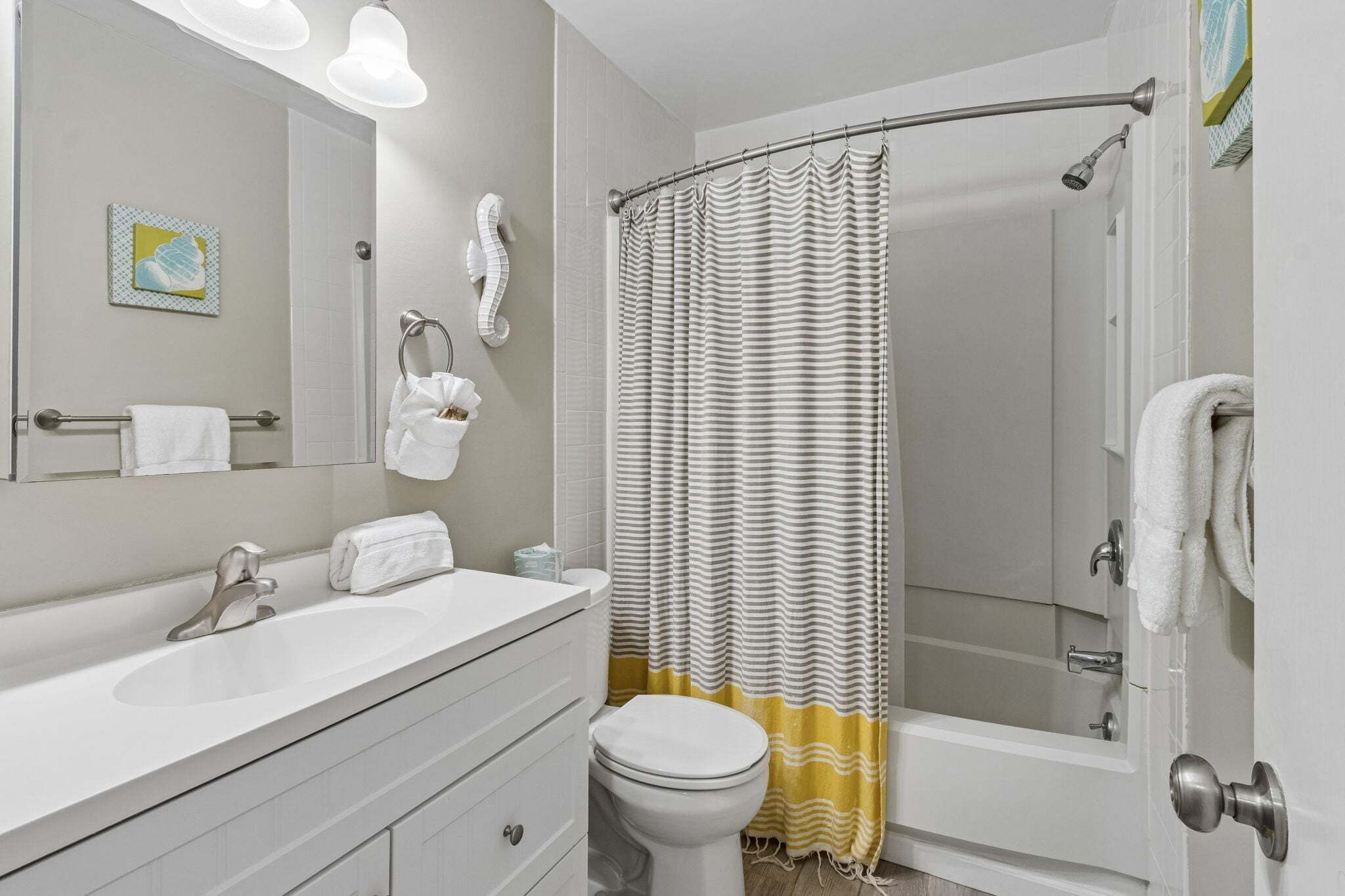 Une salle de bain avec un lavabo blanc, des toilettes, une douche avec un rideau à rayures et un porte-serviettes.