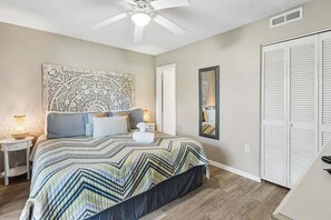 A bedroom with a bed, a ceiling fan, a nightstand, a bedside lamp, a mirror, and a closet. - 2 blocks to the beach! Elegant Second floor 2 BR/2 BA - Secluded Lanai, WiFI, Pool & Tennis (Fernandina Beach)
