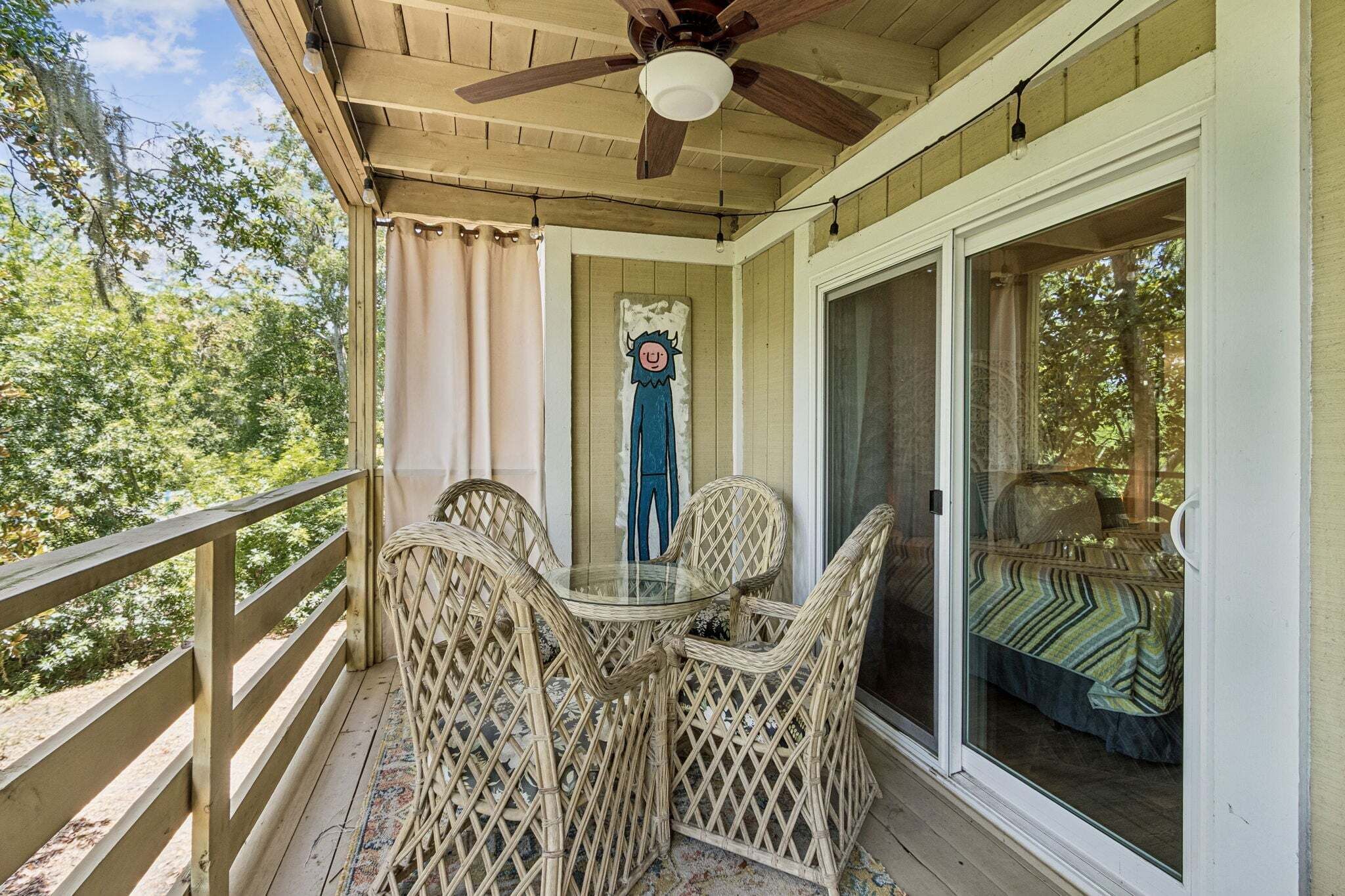 A covered porch with wicker chairs, a glass table, and a ceiling fan.