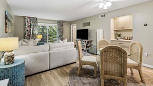 Un salon comprenant un canapé, un téléviseur, des fauteuils en osier et un ventilateur de plafond.