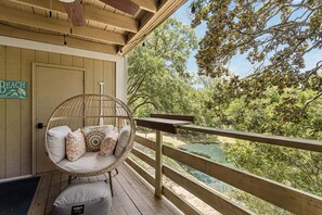 Une terrasse en bois avec une chaise en osier et des coussins, donnant sur un paysage naturel composé d’arbres et d’une étendue d’eau.
