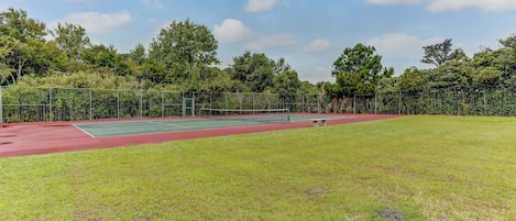 A tennis court with a surrounding grassy area and trees.
