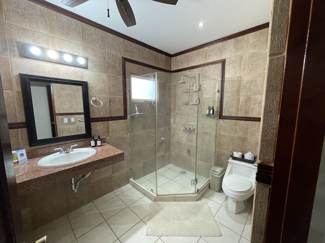 Un baño moderno con ducha de vidrio, lavamanos con espejo e inodoro.